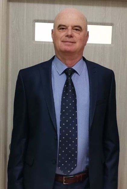 Man in a suit and tie standing indoors, posing for a photo with a neutral expression.